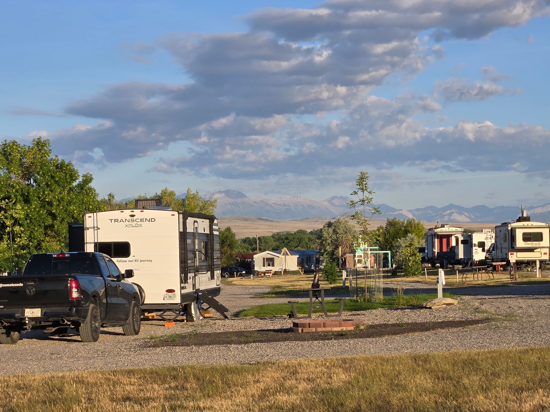 Campground with RVs and a truck; mountains in the distance under a cloudy sky.