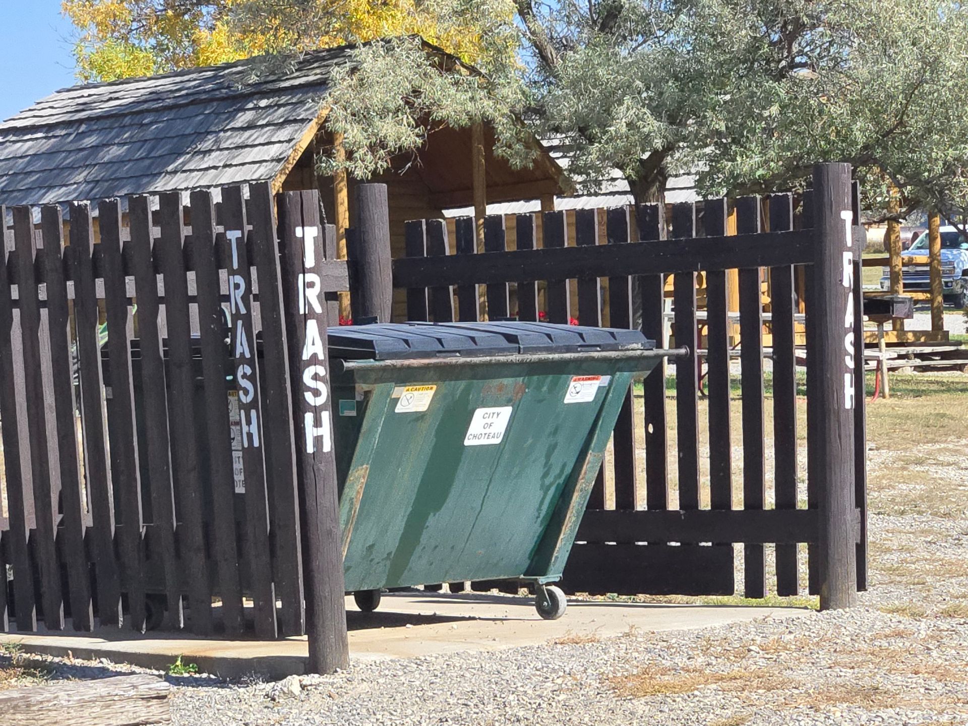 Green dumpster within a wooden enclosure, labeled 