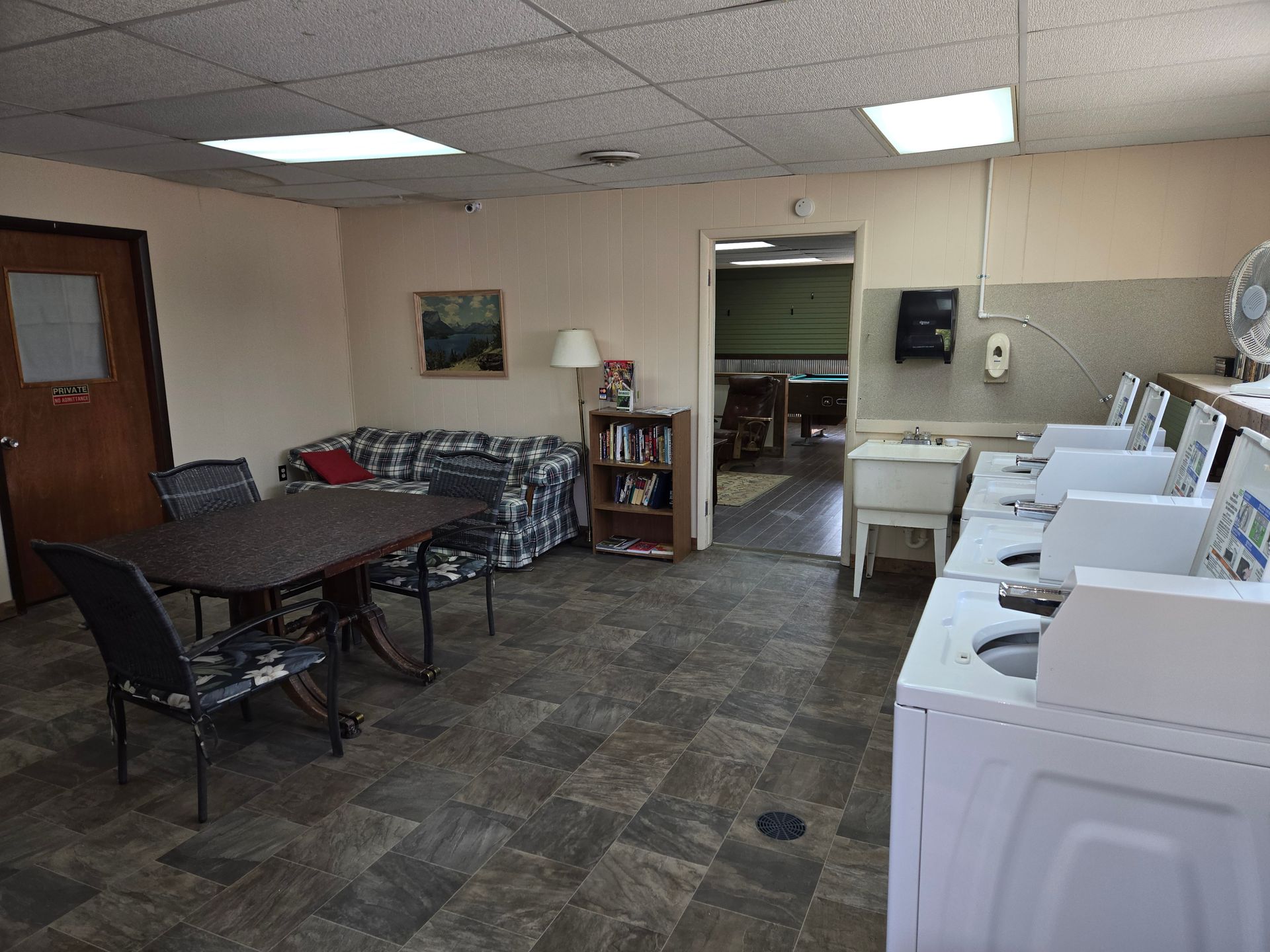 Laundry room: washers, dryer, table with chairs, couch, bookshelf, sink, doorway.