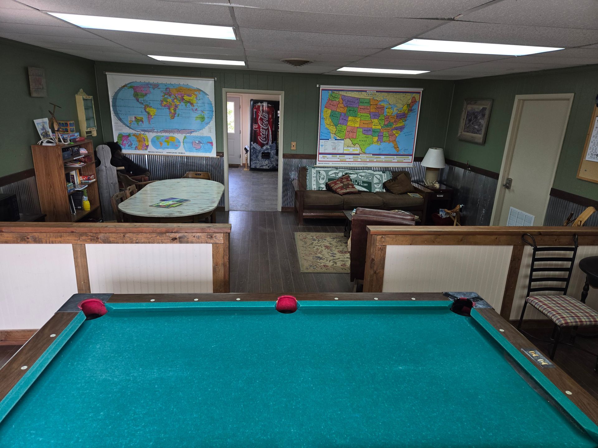 Pool table in a game room with maps, furniture, and a doorway.