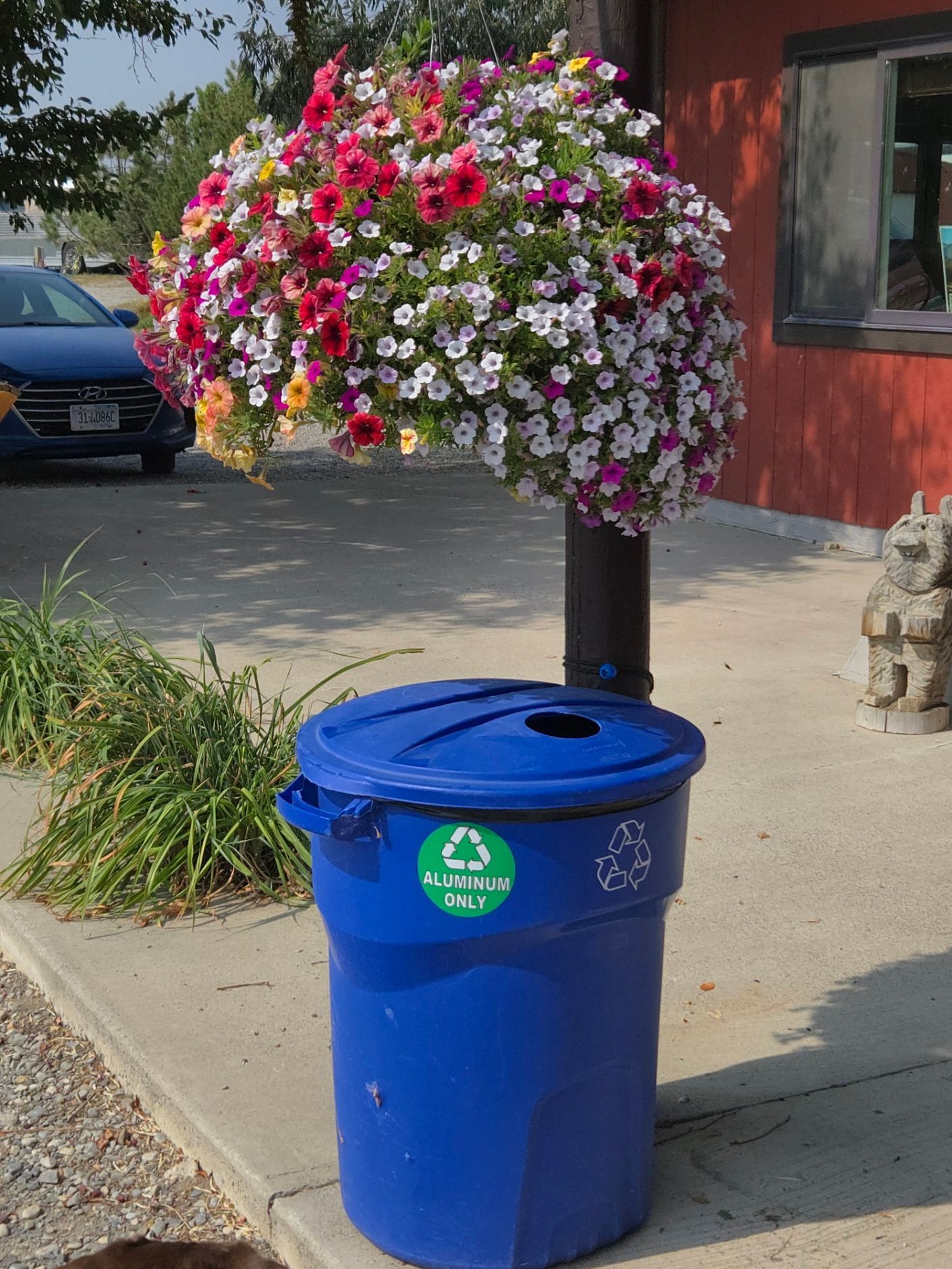 Blue recycling bin with a floral display on a black pole; a car and building are in the background.