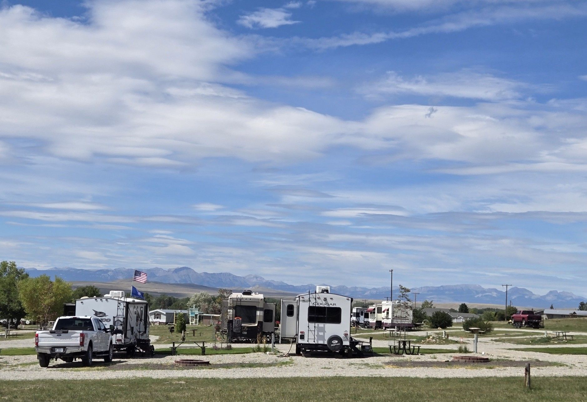 RV park with campers under a blue sky, mountains in the distance.