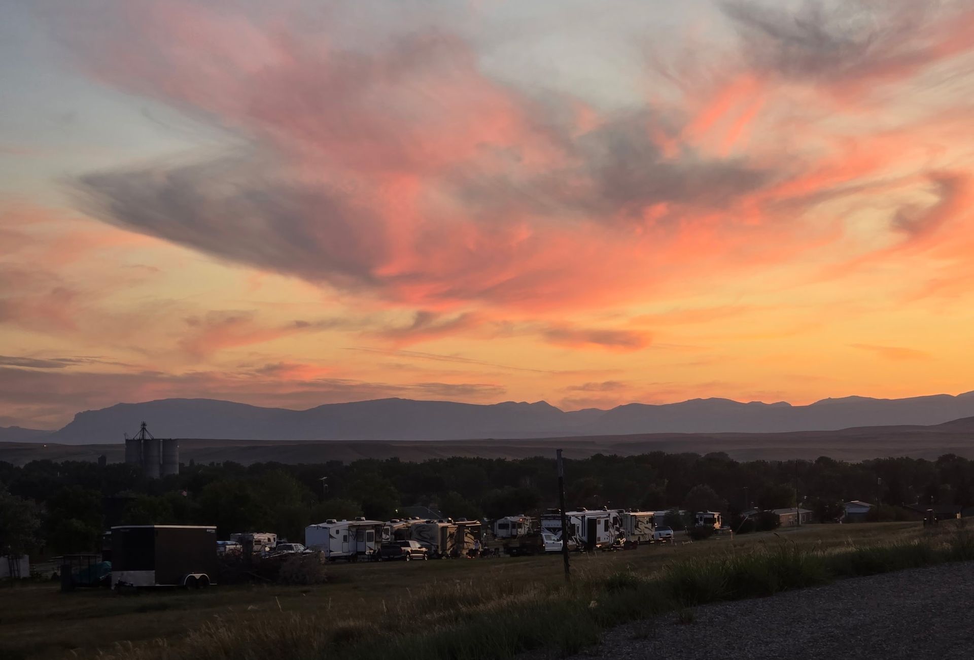 Sunset over a campground with RVs and mountains in the distance; orange and pink sky.
