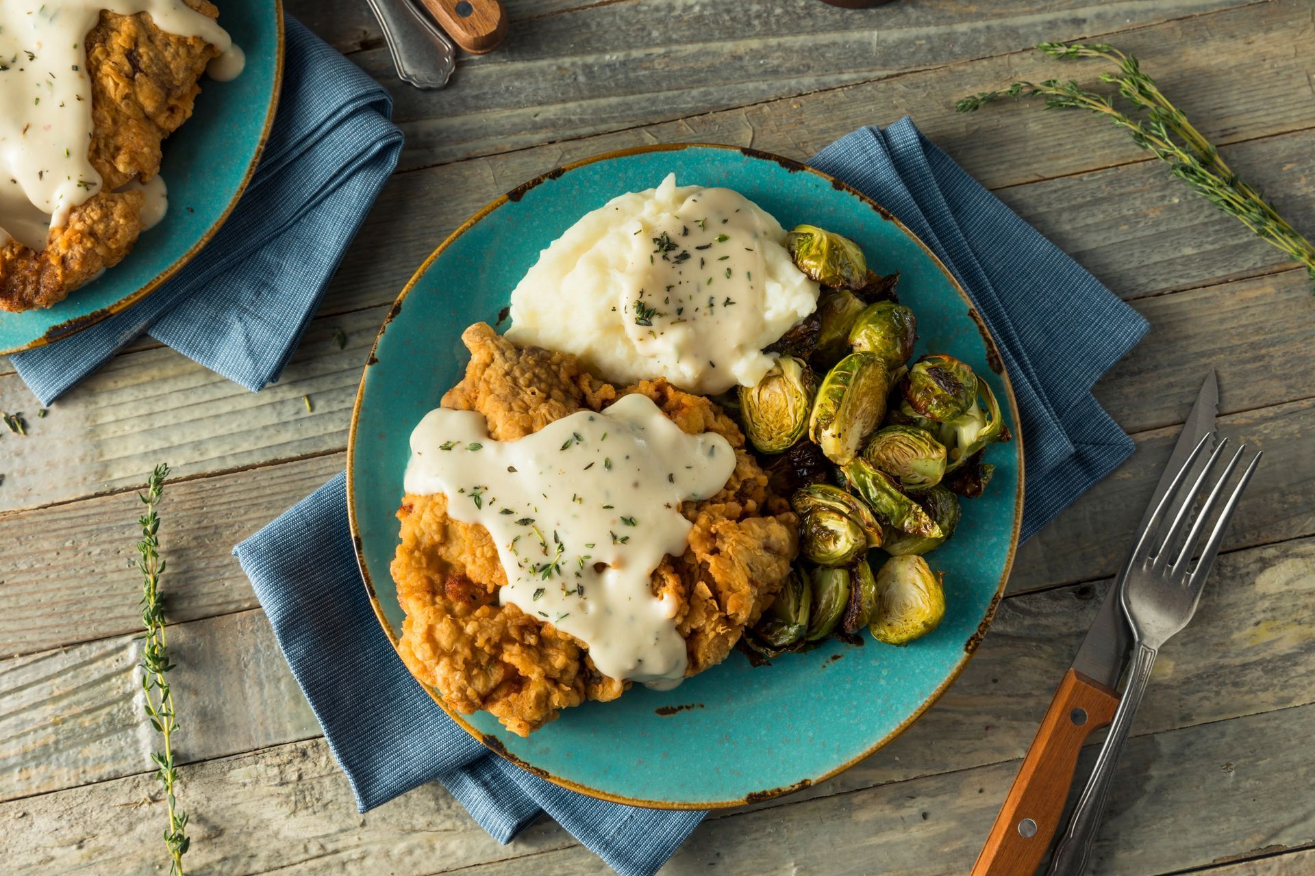 Chicken fried steak with mashed potatoes and Brussels sprouts on a blue plate.