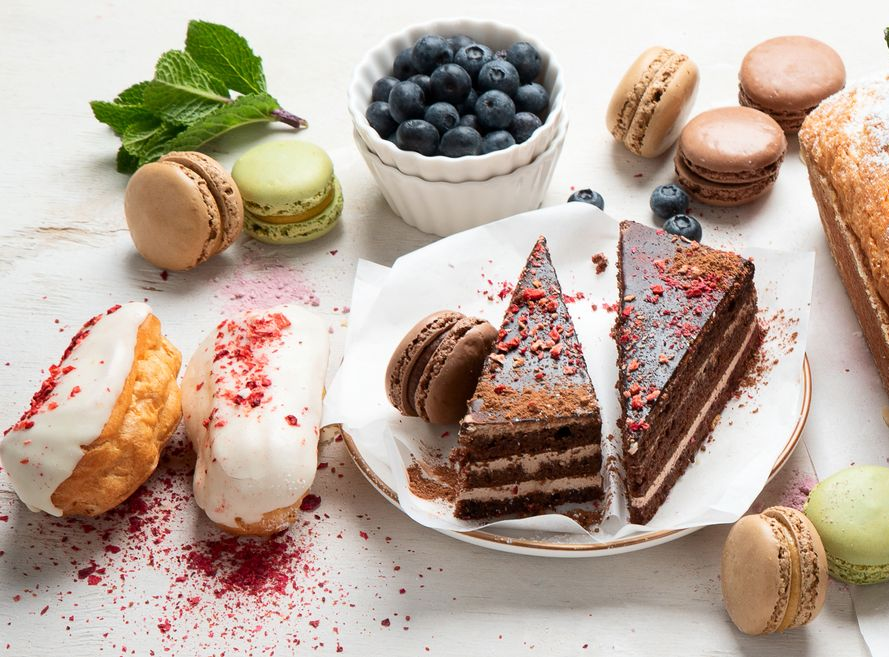 Desserts: chocolate cake, macarons, cream puffs, and blueberries on a white surface.
