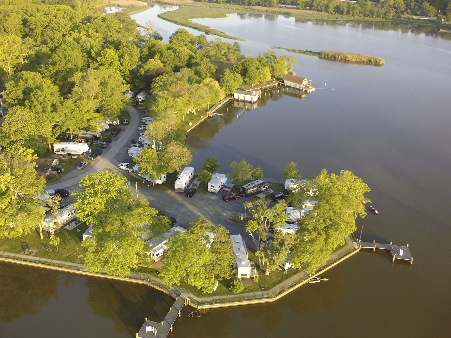Aerial view of a wooded lakeside campsite with RVs, roads, docks, and calm water.