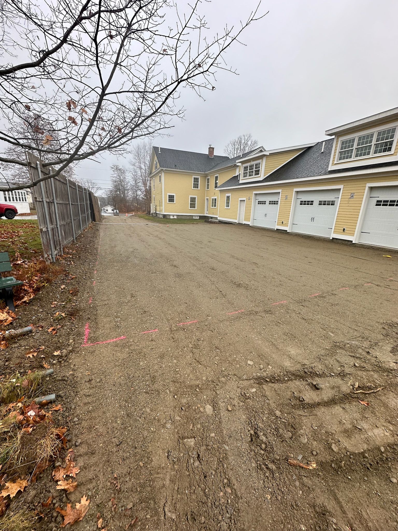 A dirt road leading to a row of garages next to a house.