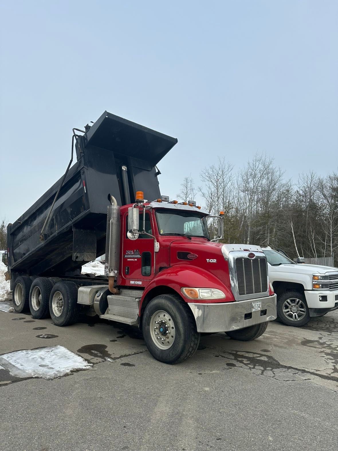 A red dump truck is parked on the side of the road next to a white truck.