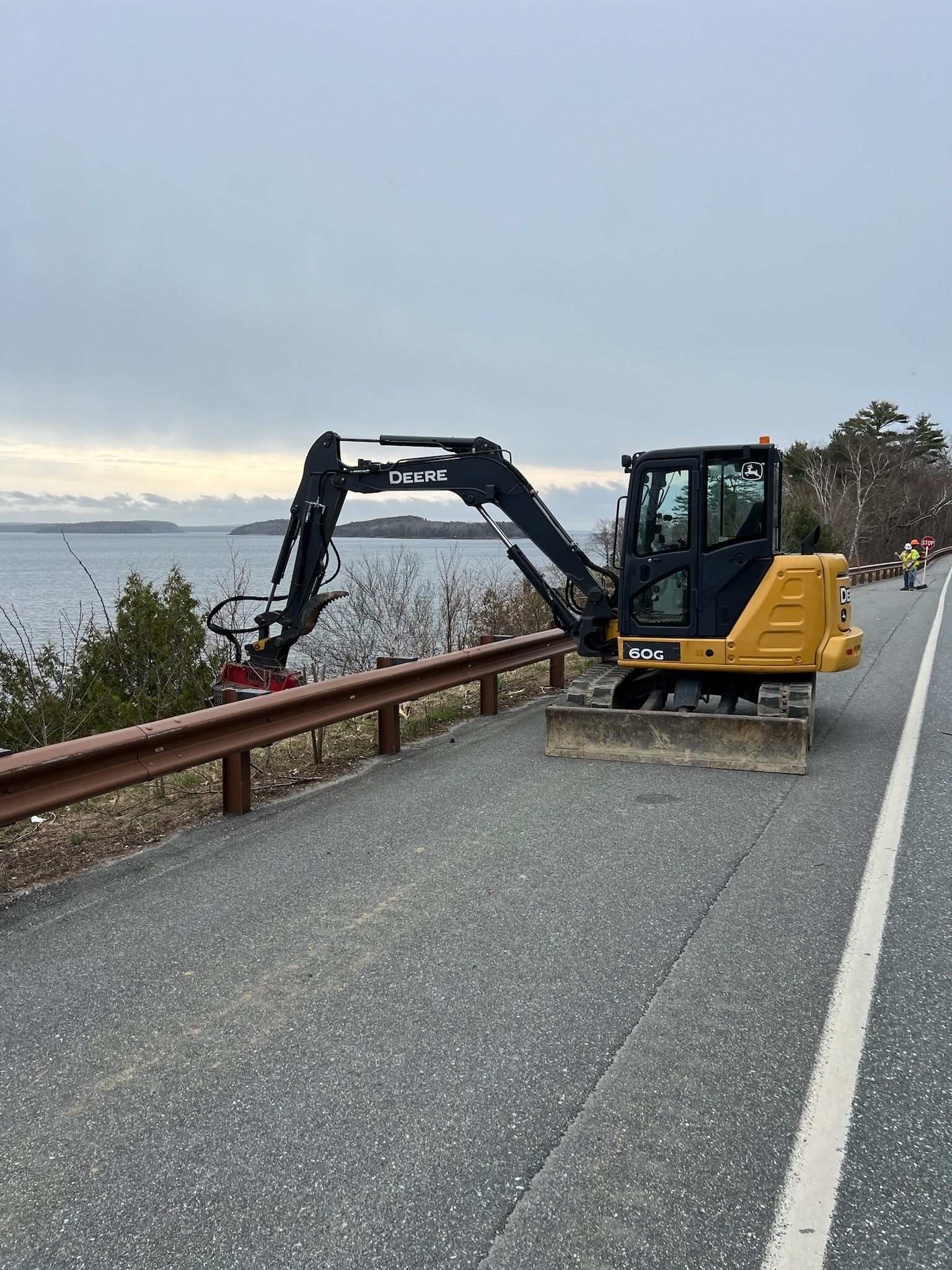A yellow excavator is sitting on the side of a road next to a body of water.