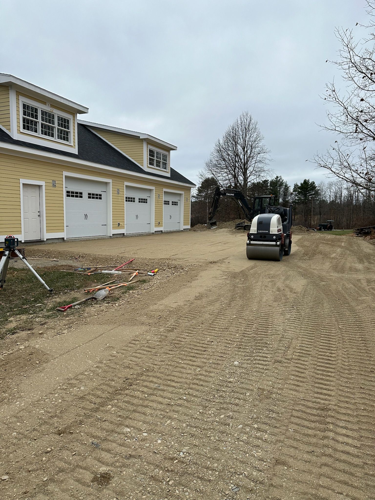 A construction vehicle is driving down a dirt road in front of a house.