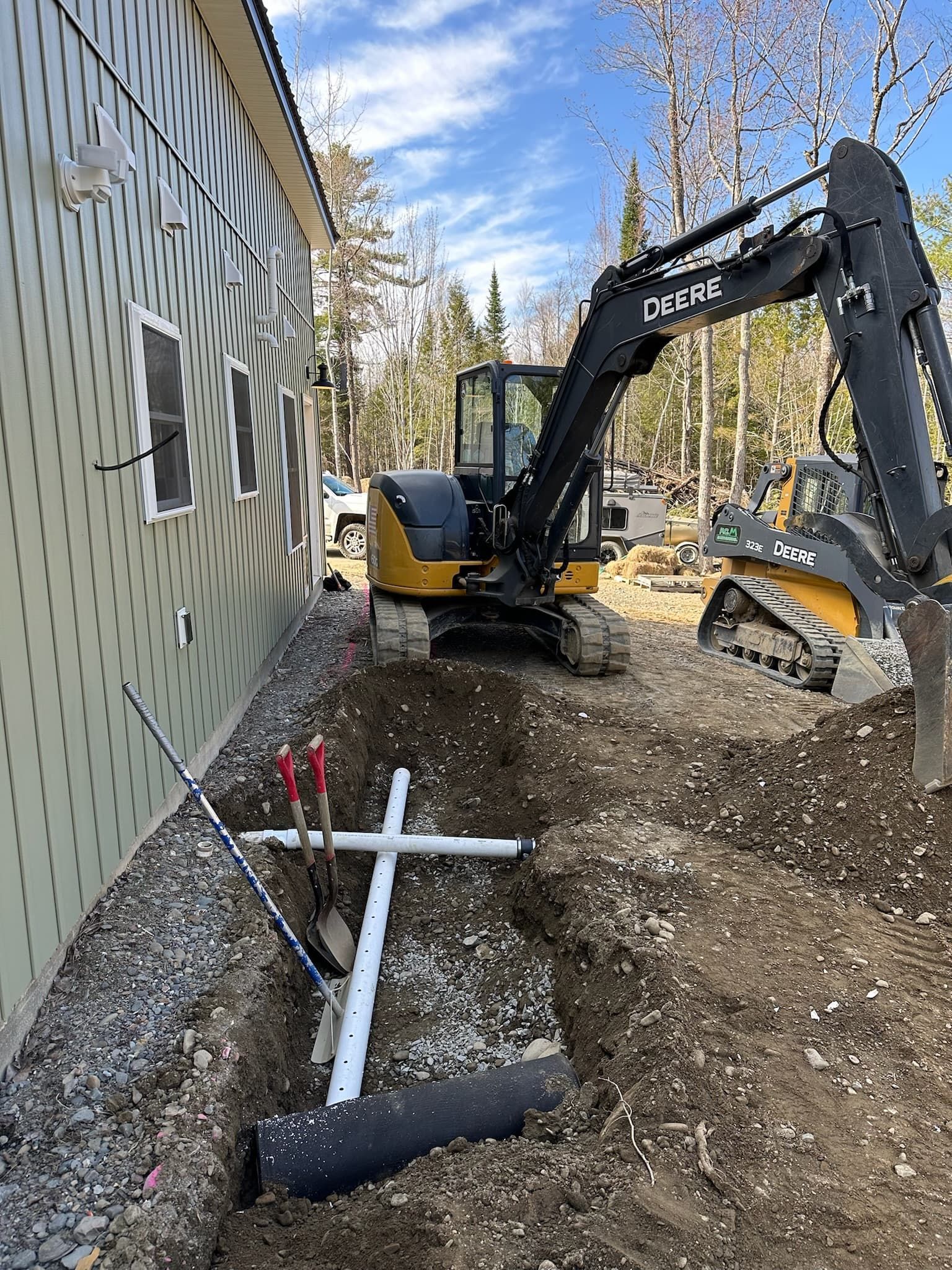 An excavator is digging a hole in the dirt in front of a house.
