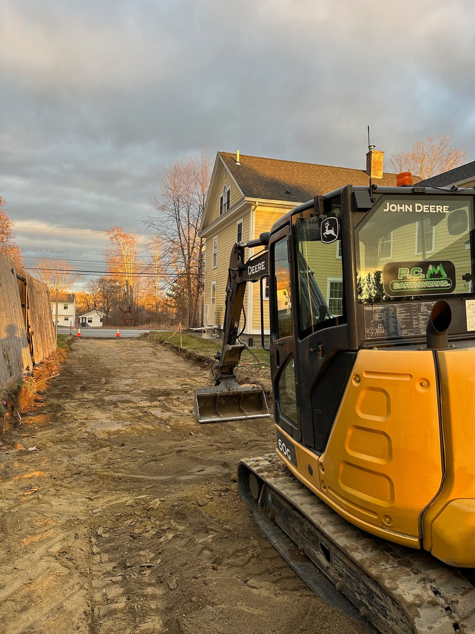 A yellow excavator is driving down a dirt road in front of a house.