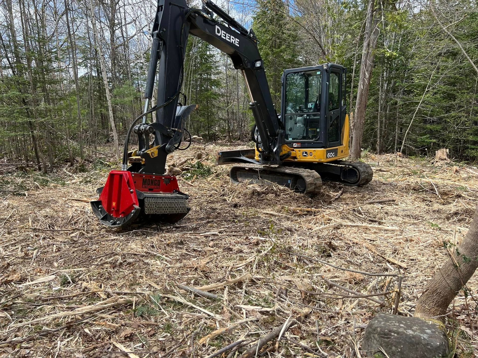 A large excavator is cutting down trees in the woods.