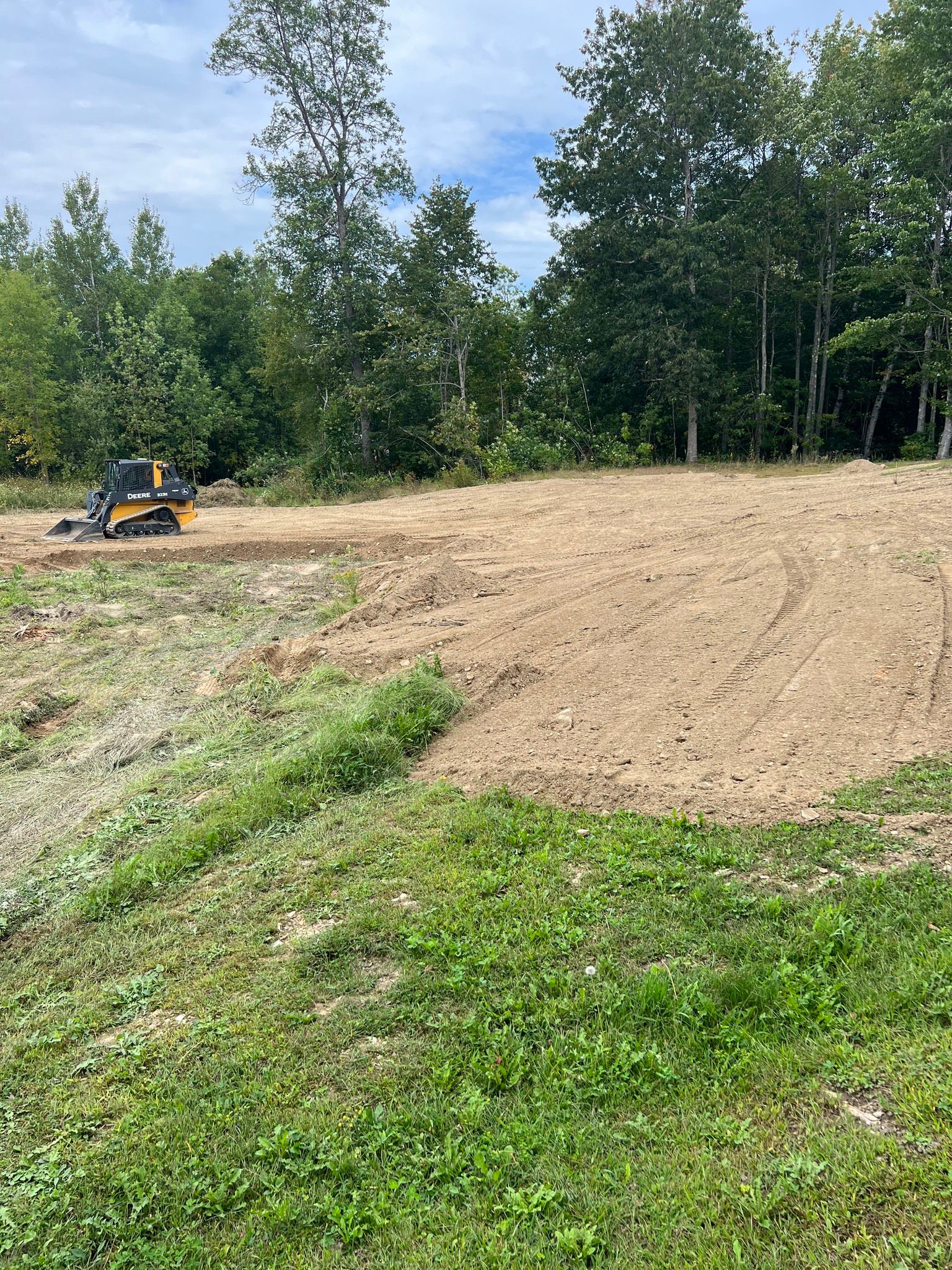 A large dirt field with trees in the background and a bulldozer in the middle of it.
