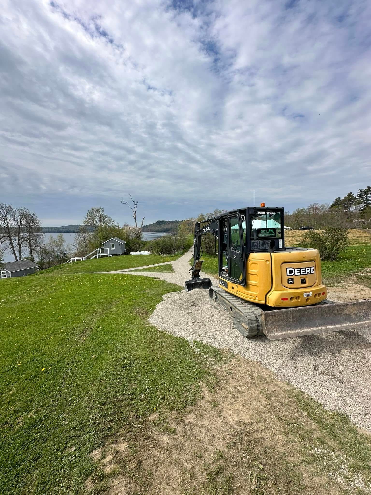 A yellow excavator is parked in a grassy field next to a body of water.
