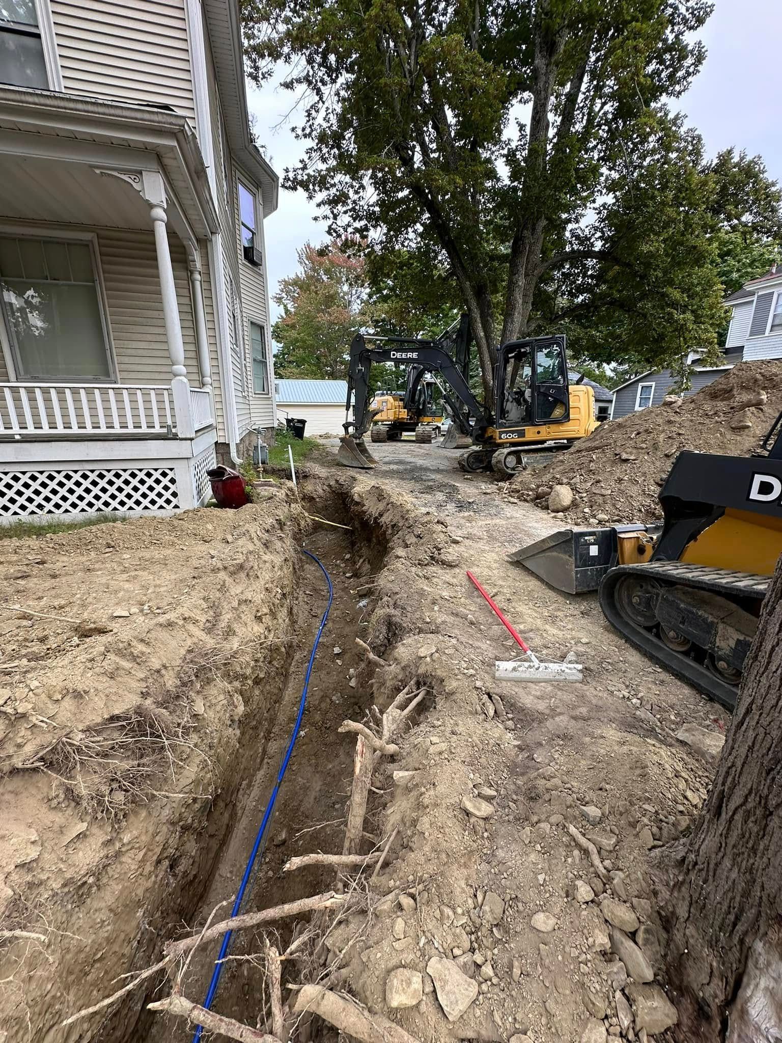 A large excavator is digging a trench in front of a house.