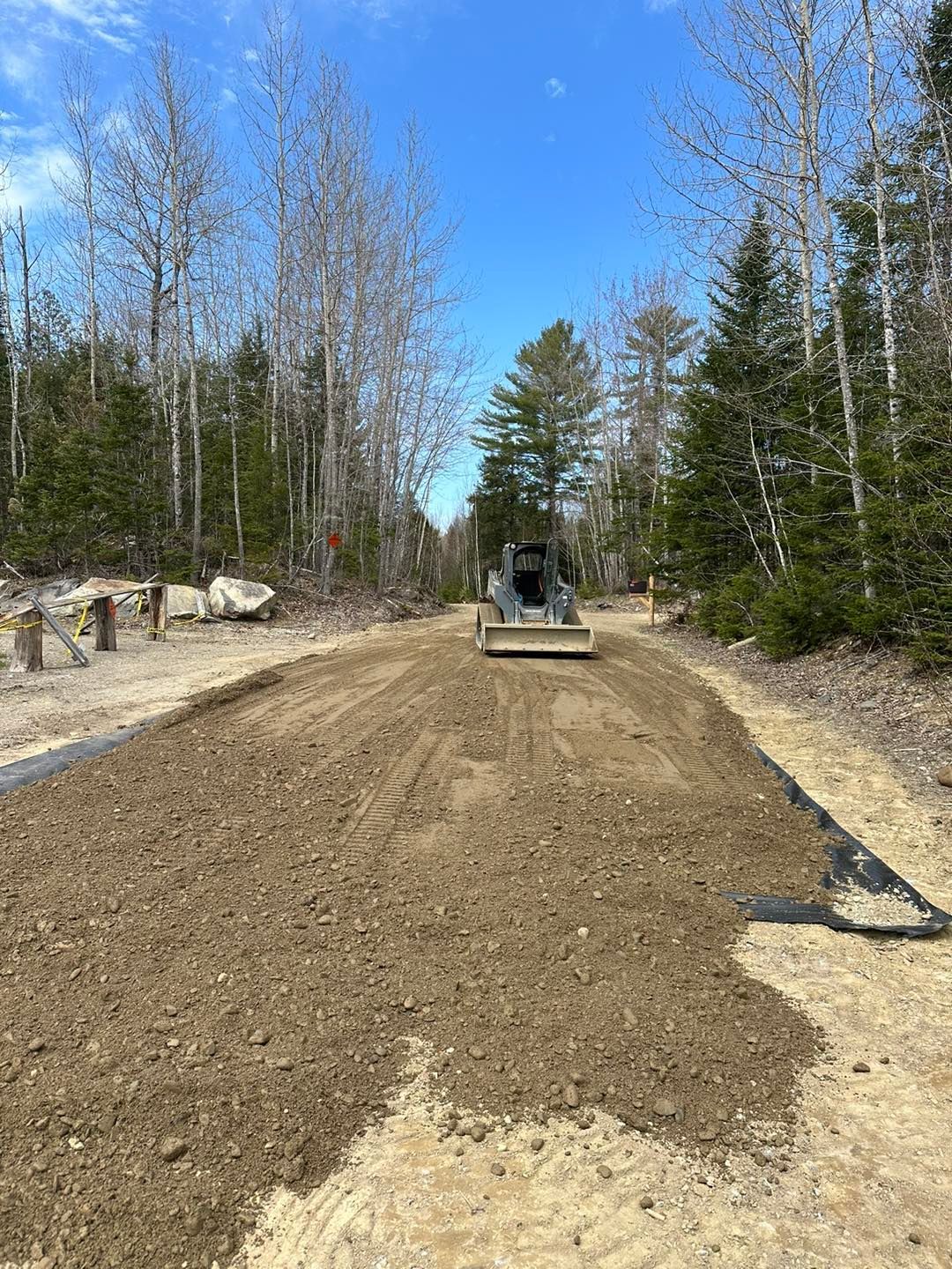 A bulldozer is moving dirt on a dirt road in the woods.