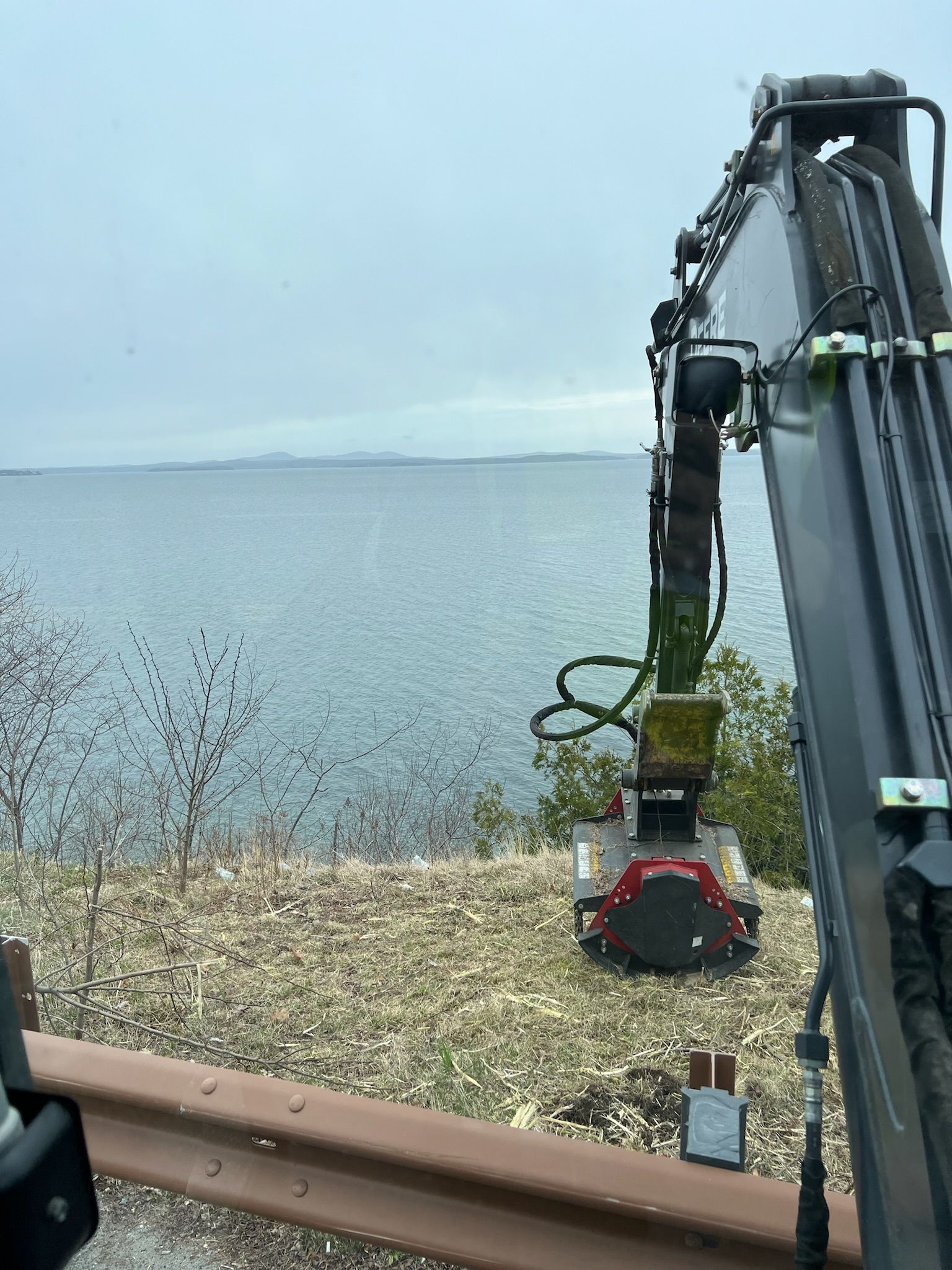 A crane is sitting on the side of a road next to a body of water.