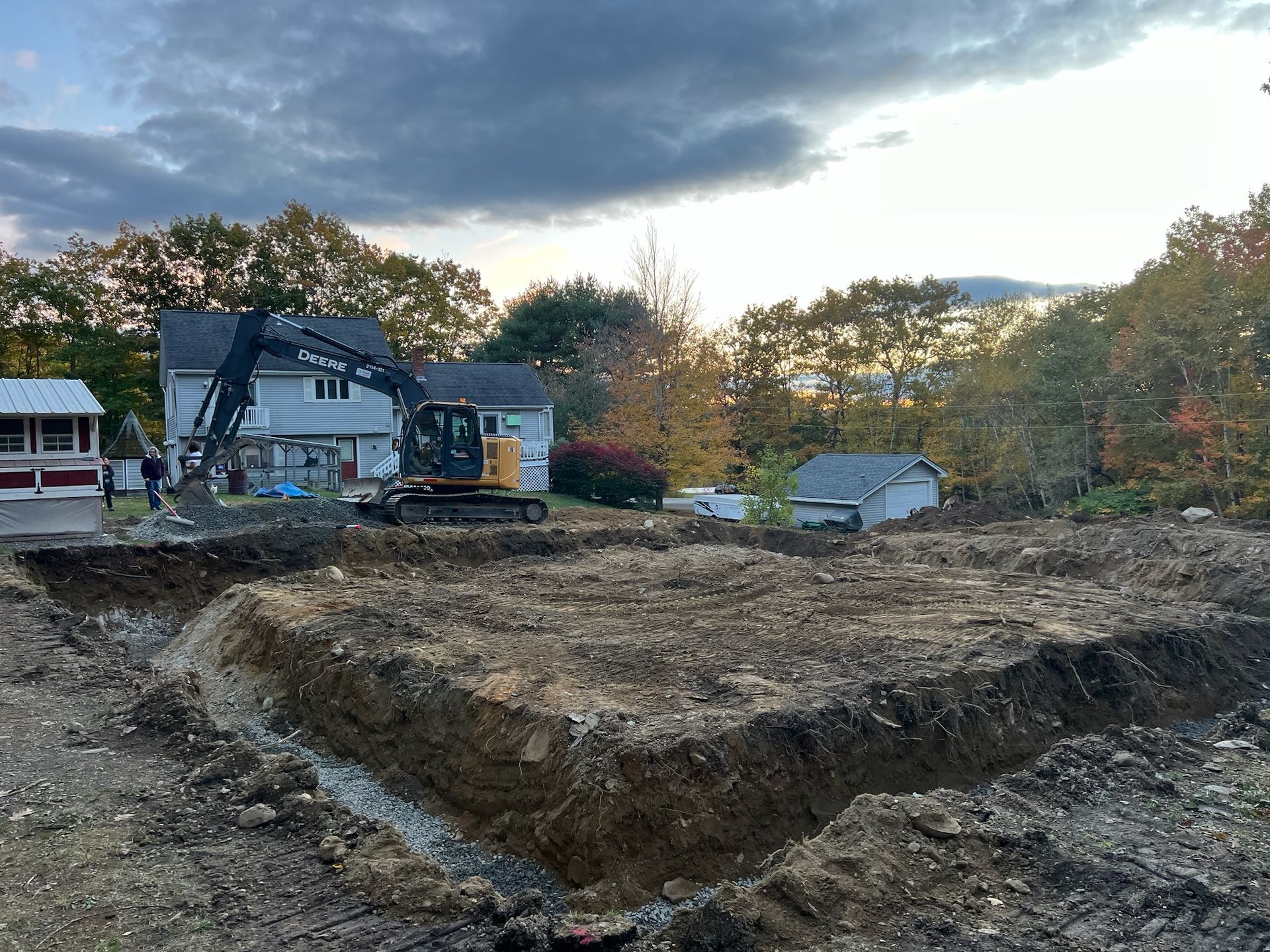 A large excavator is digging a hole in a dirt field in front of a house.