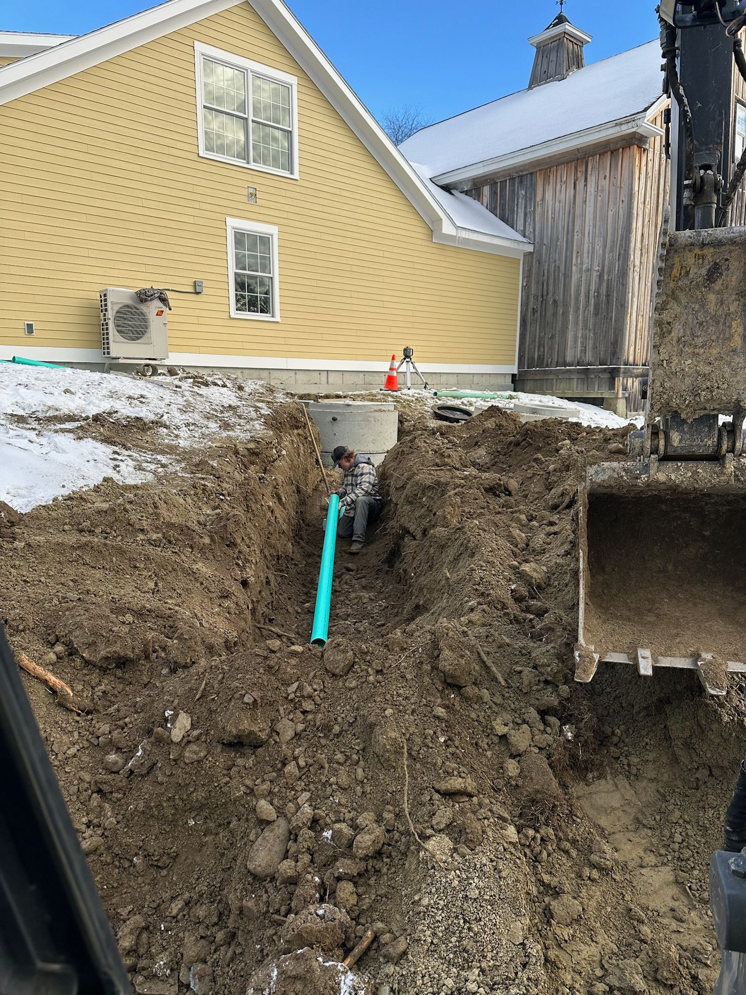A green pipe is being installed in the dirt in front of a house.
