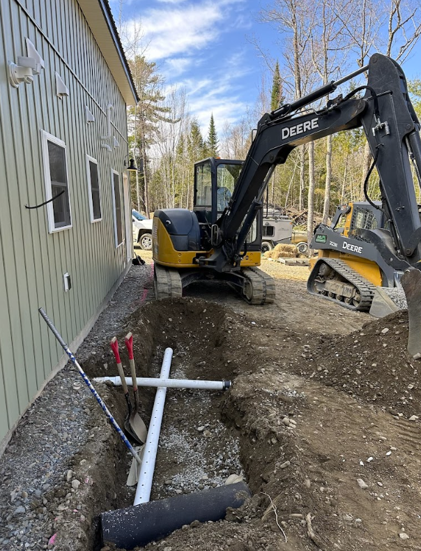 An excavator is digging a hole in the ground next to a house.