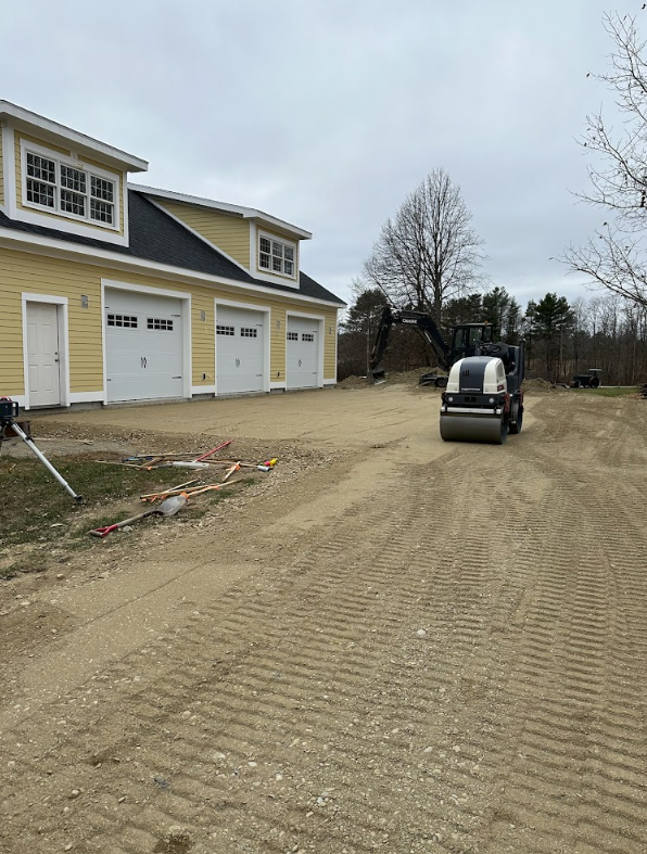 A tractor is driving down a dirt road in front of a house.