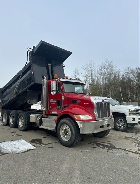 A red dump truck is parked next to a white truck in a parking lot.
