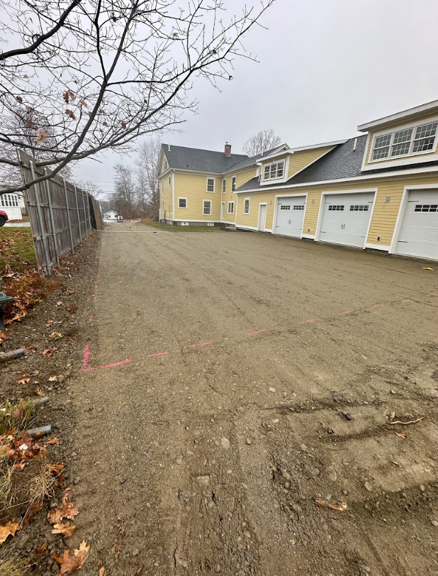 A dirt road leading to a house with garage doors.