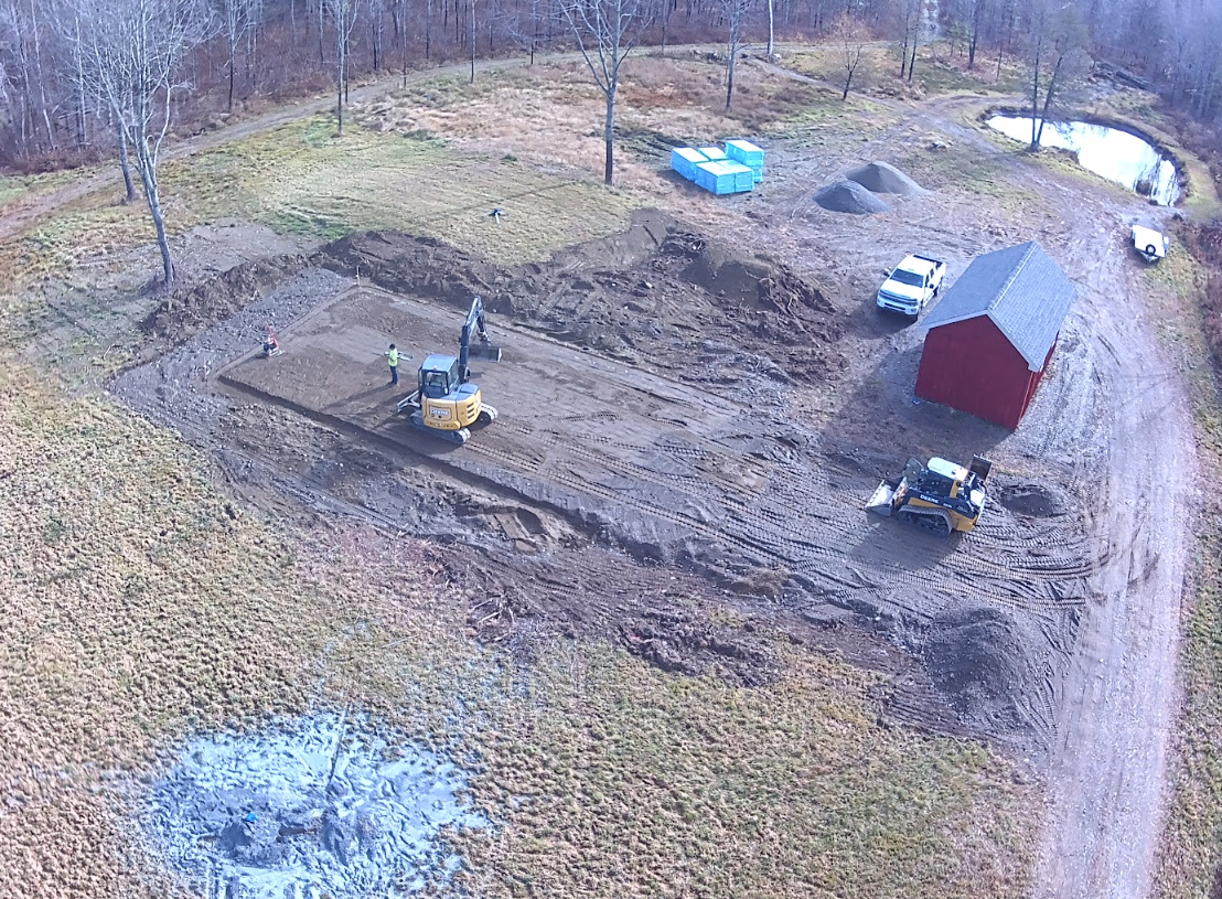 An aerial view of a dirt road with a red barn in the background.