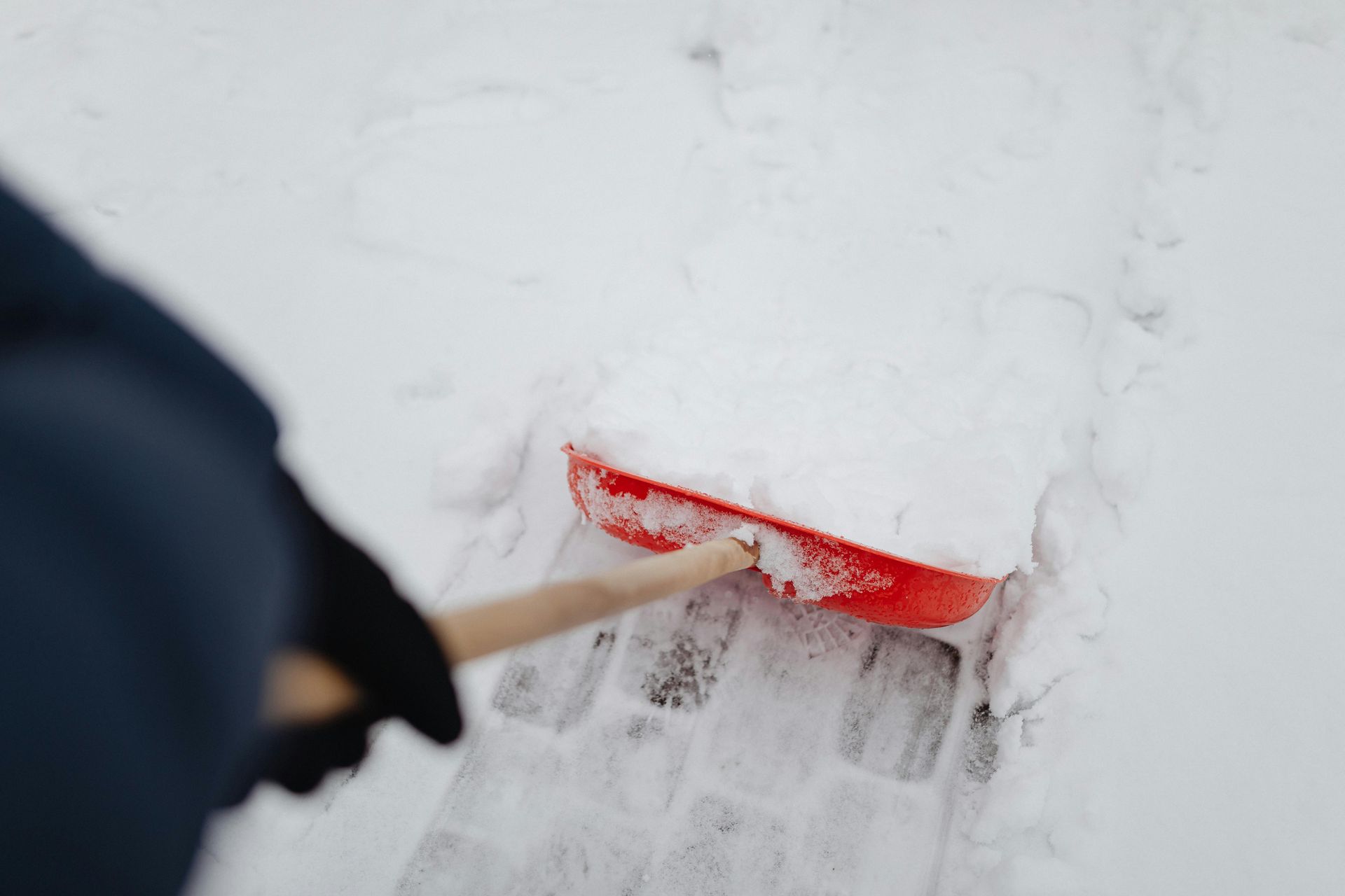 A person is shoveling snow with a red shovel.