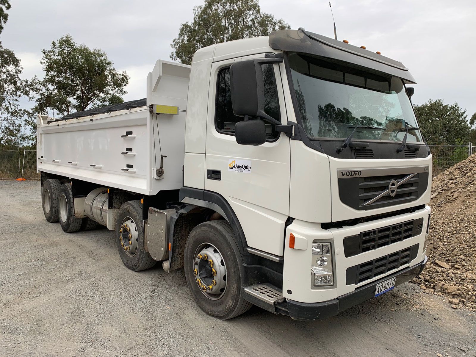 A white dump truck is parked in a dirt lot next to a pile of dirt.