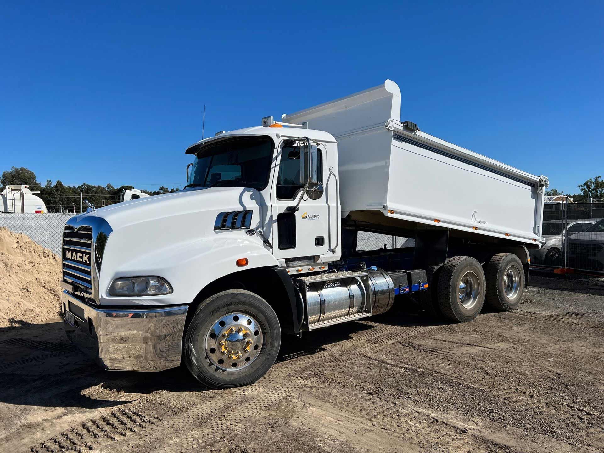 A white dump truck is parked in a dirt lot next to a pile of dirt.