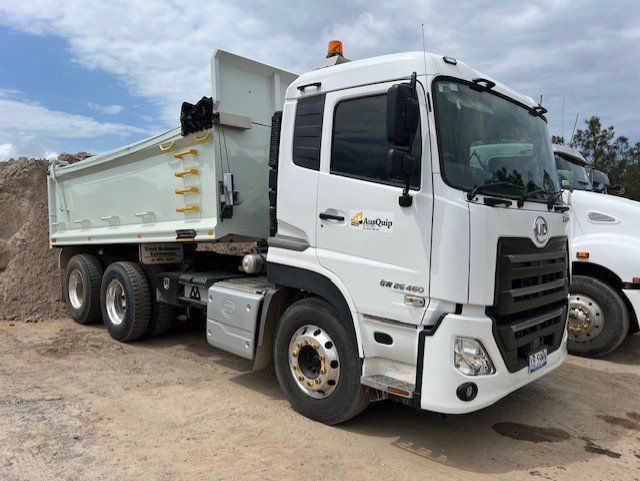 A white dump truck is parked in front of a pile of dirt.