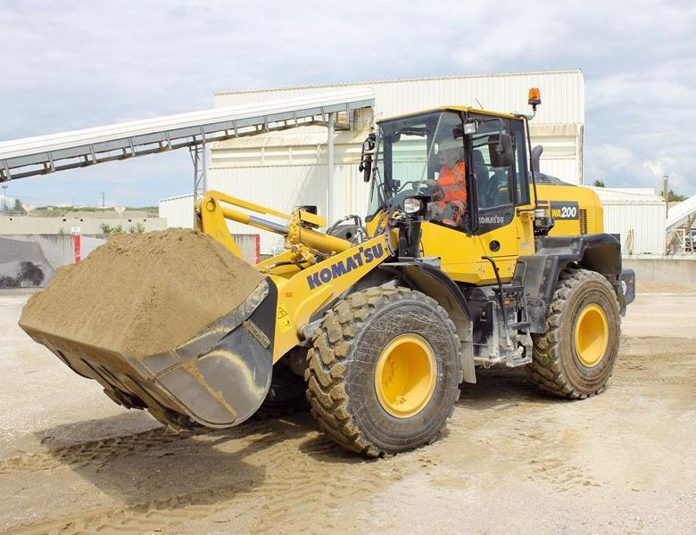 A yellow komatsu wheel loader is loading sand into a bucket.