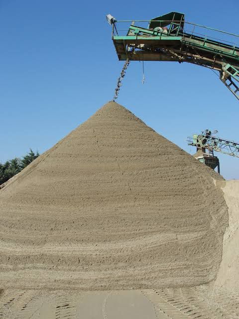 A large pile of sand is being poured from a conveyor belt