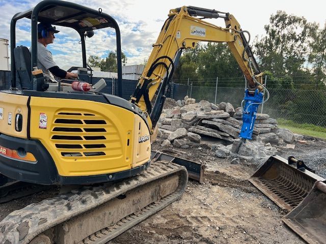 A man is driving a yellow excavator on a construction site.
