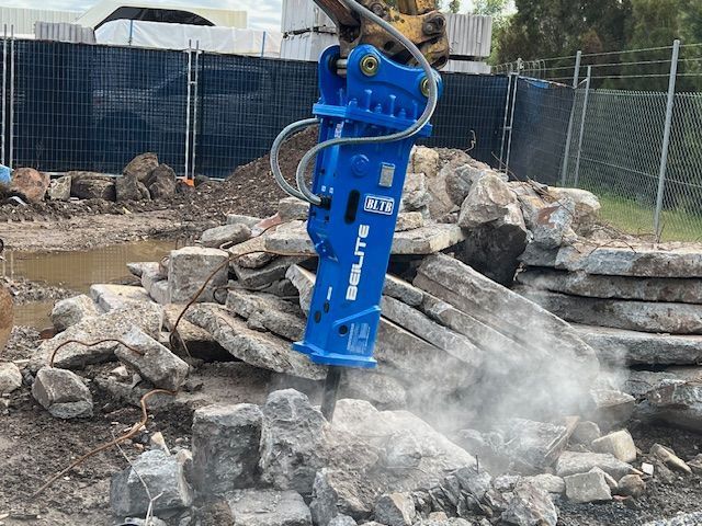 A blue hydraulic hammer is breaking rocks on a construction site.