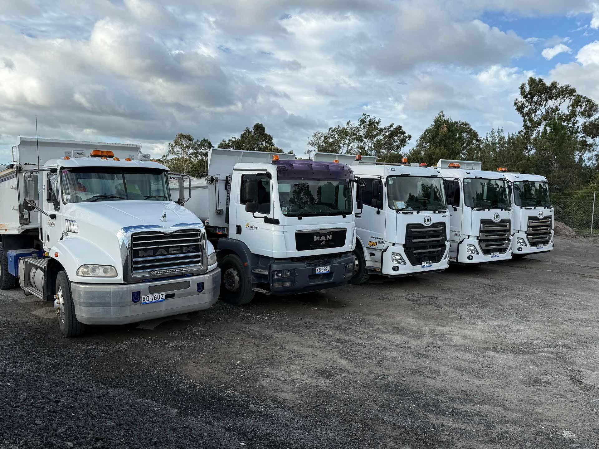 A row of dump trucks are parked in a gravel lot.