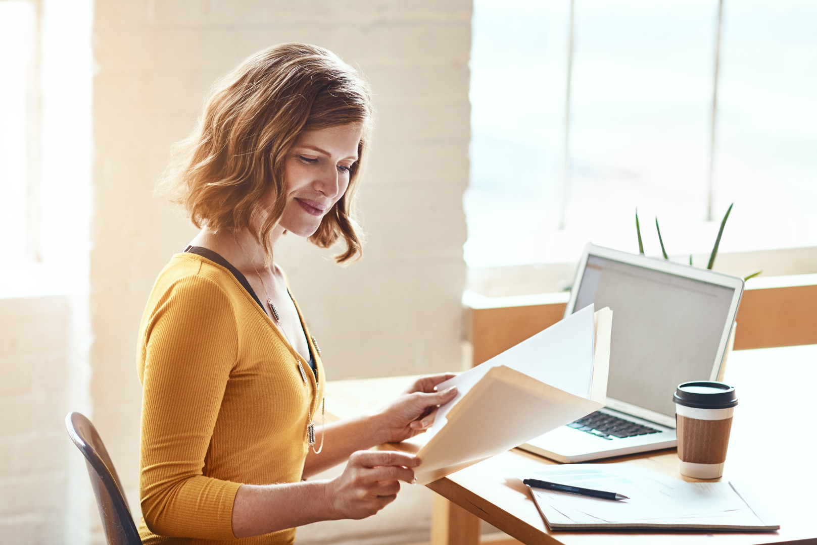 A woman is sitting at a desk looking at a piece of paper.