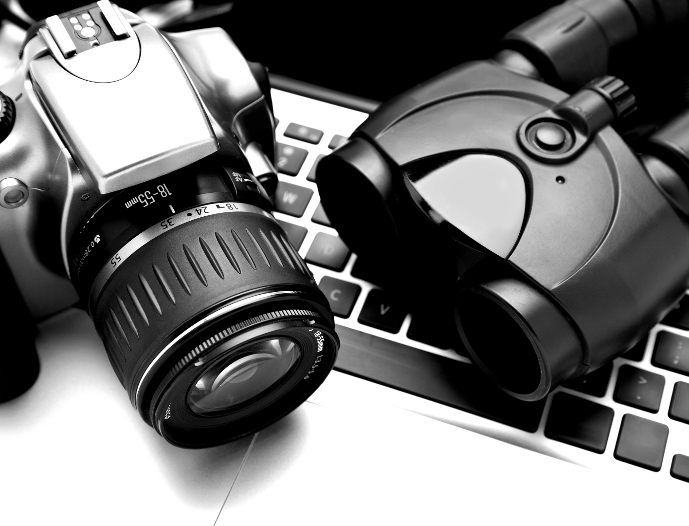 A camera and binoculars are sitting on top of a keyboard