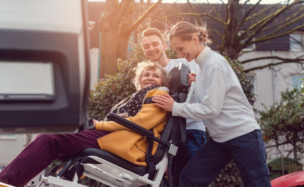 Two Helpers Picking Up Disabled Senior Woman In Wheelchair For Transport — Shuttle Buses from Hervey Bay in Dundowran Beach, QLD