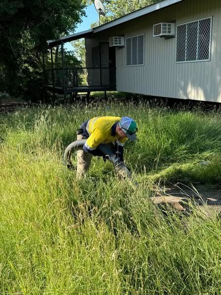 A Man is Kneeling in the Grass in Front of a House — Ecotreat Solutions NT in Winnellie, NT