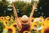 Person in straw hat raising arms in a sunflower field with floating bubbles