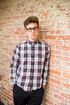 Person in glasses and plaid shirt leaning against a brick wall.