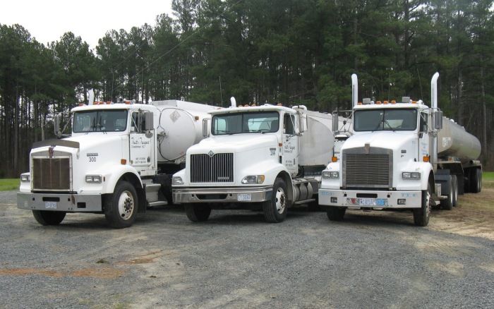 Three white cement mixer trucks parked side by side on a gravel lot