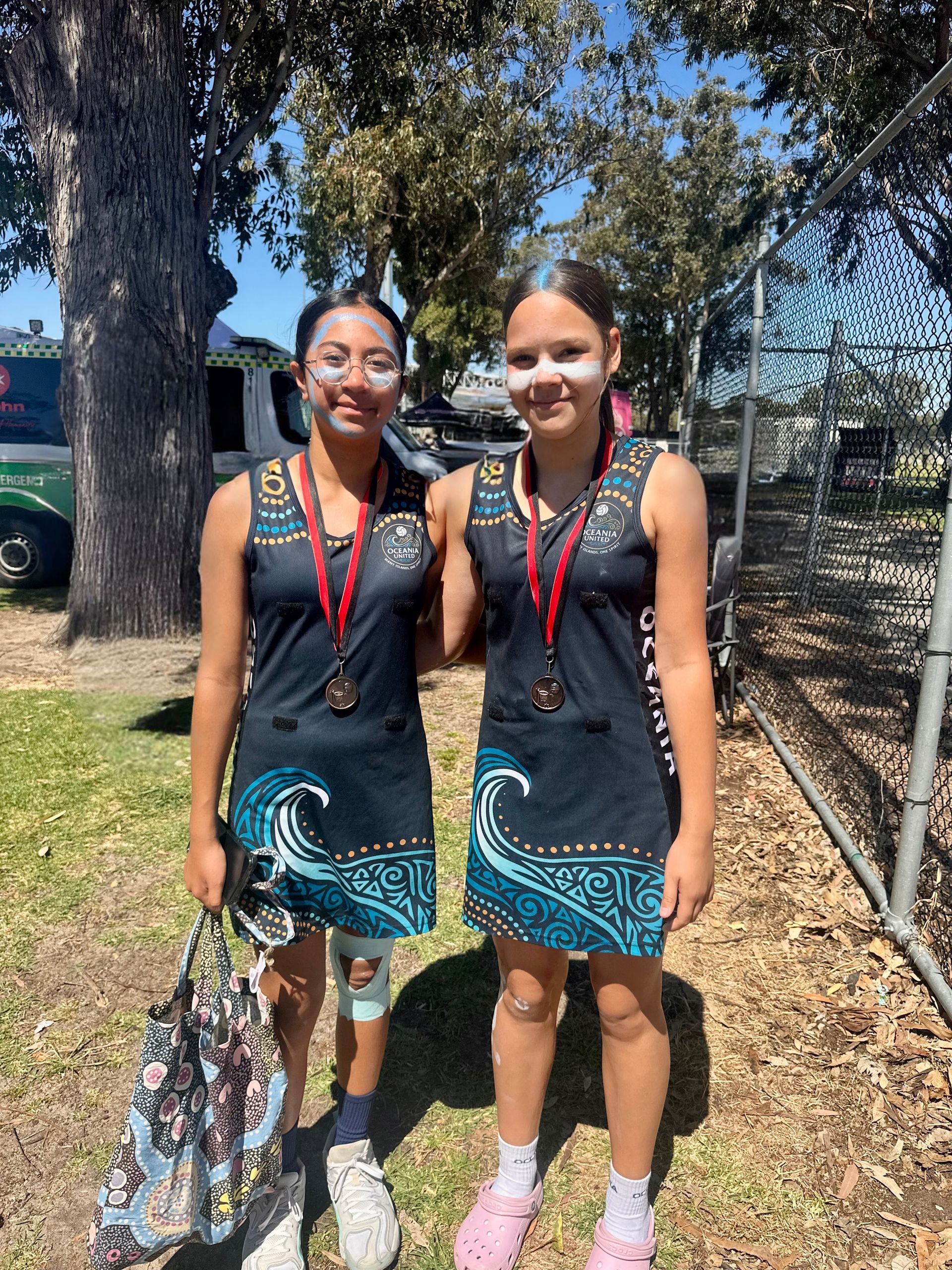 Two young people wearing matching dresses with medals posing outdoors.