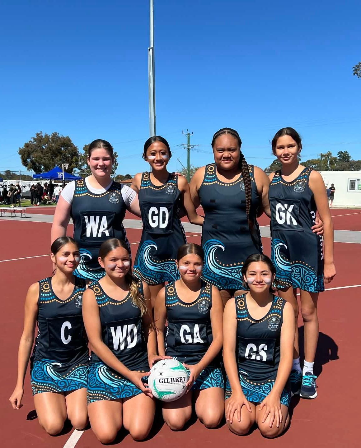 Netball team posing on a red court, wearing matching blue and white uniforms.