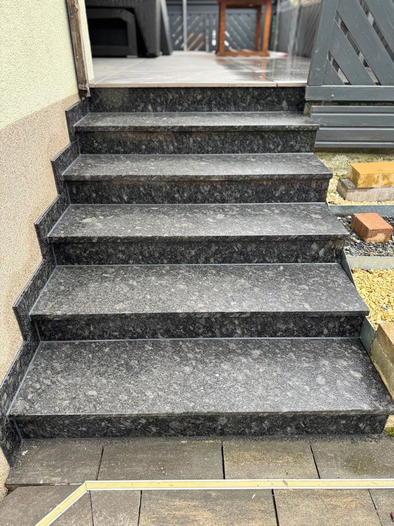 Steintreppe, die zu einem Türrahmen führt; dunkelgrauer Granit mit gesprenkeltem Muster.