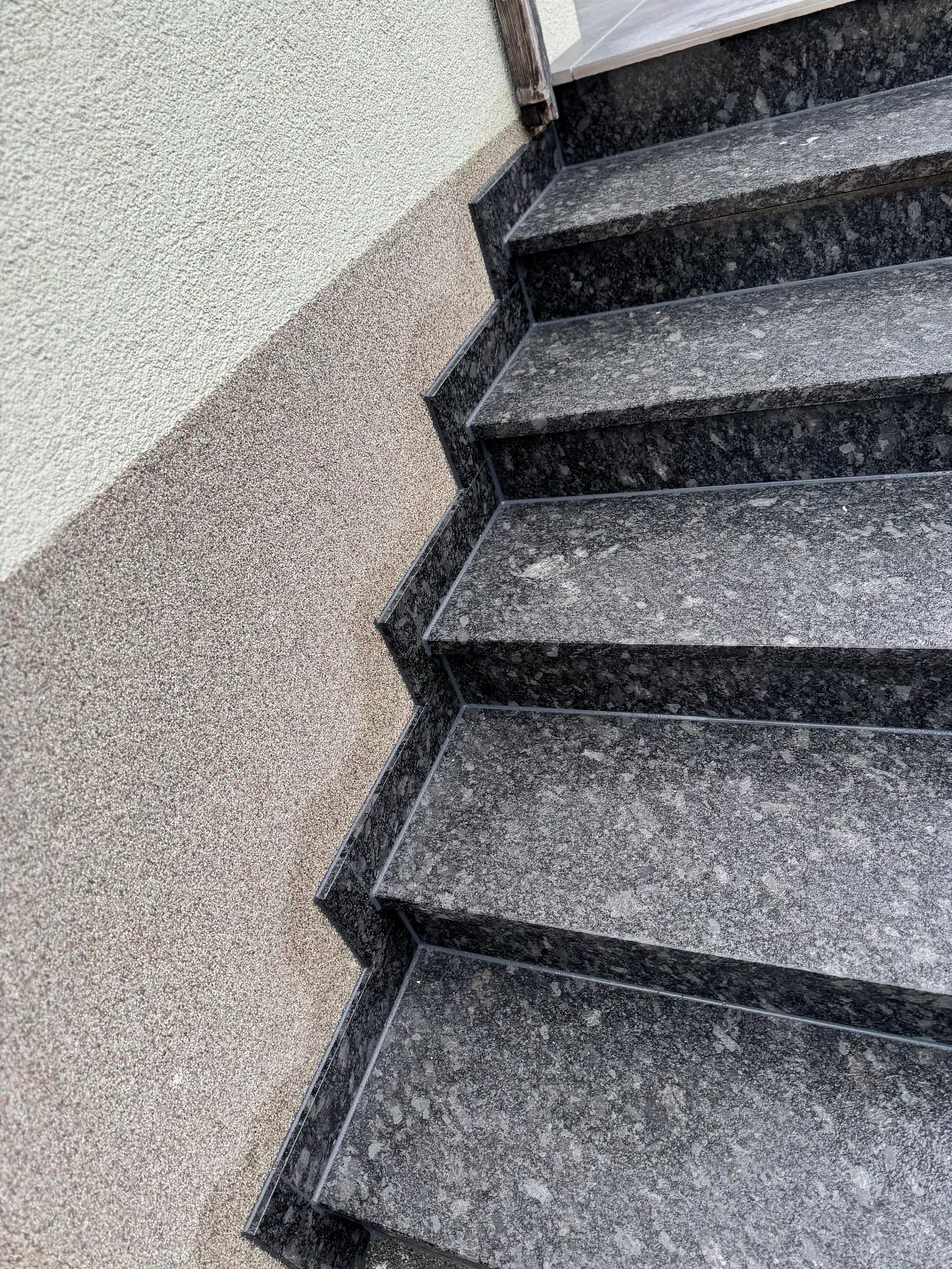 Außentreppe aus Granit neben einer strukturierten beigefarbenen Wand.