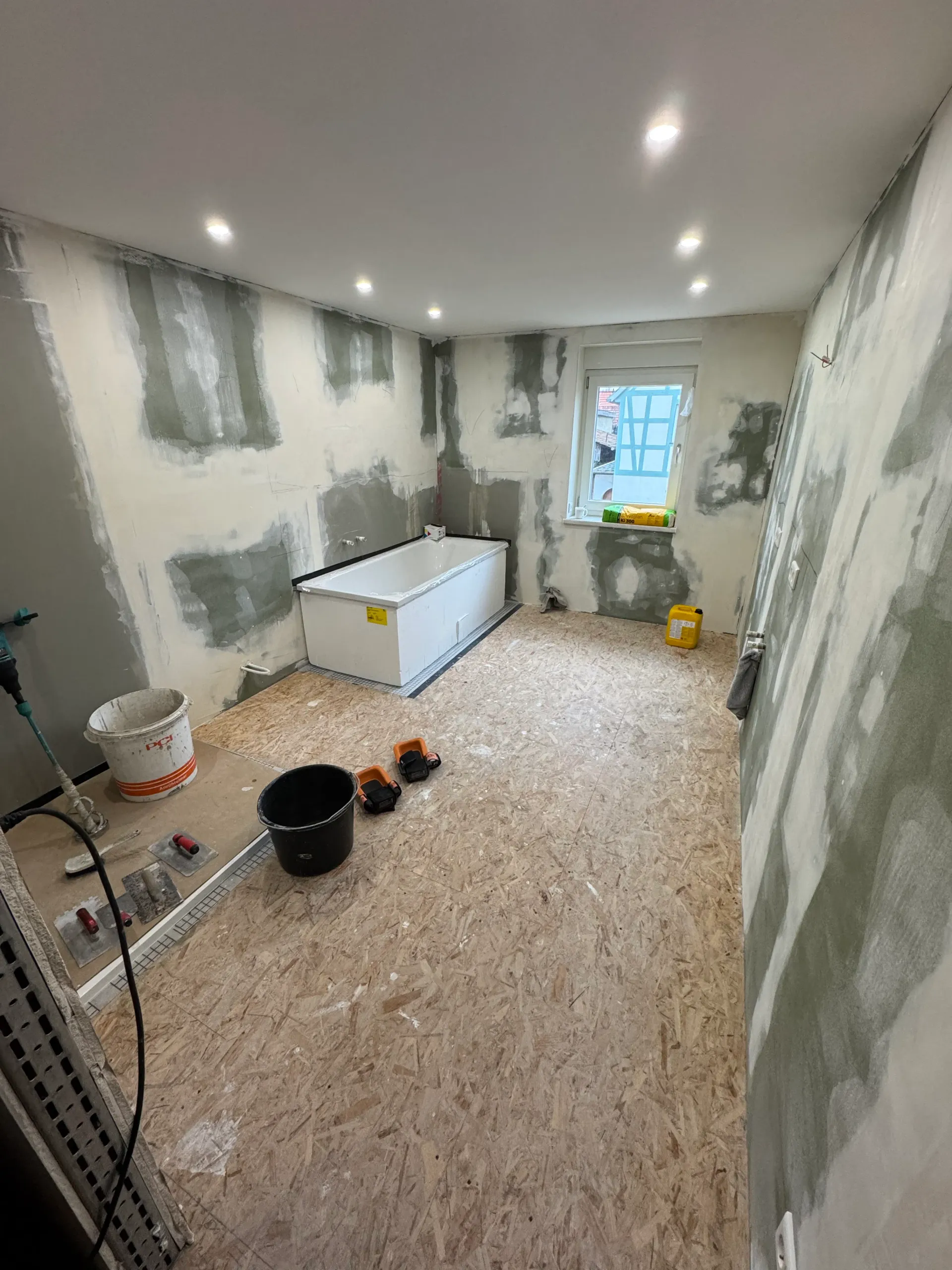 Badezimmer wird renoviert mit Trockenbauwänden, Sperrholzboden und einer Badewanne.